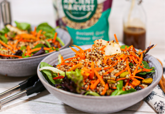 A quinoa salad in two bowls with a packaging of Ancient Harvest Harmony Quinoa in the background